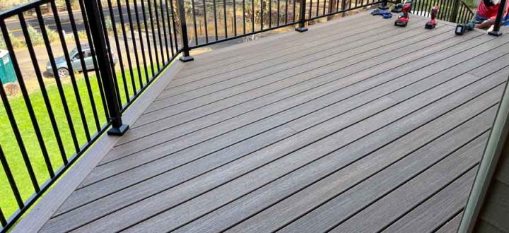 A residential deck area equipped with outdoor seating, featuring black railings and surrounded by dense forest, ideal for relaxation and entertainment.