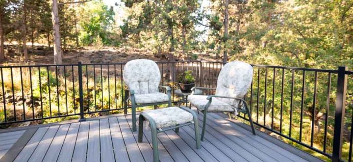 Two cozy deck chairs set against a backdrop of dense trees, offering a secluded spot for relaxation on a residential gray deck.