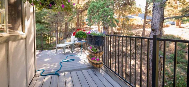 Picturesque residential deck lined with blooming flower baskets and casual outdoor seating, nestled among tall pine trees.