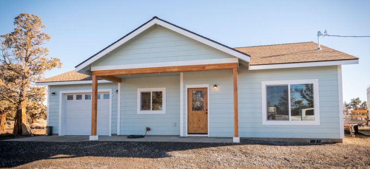 Clean, modern front view of a light blue ADU with white trim, natural wood front door, and warm outdoor sconce lighting—perfect for welcoming guests or tenants.